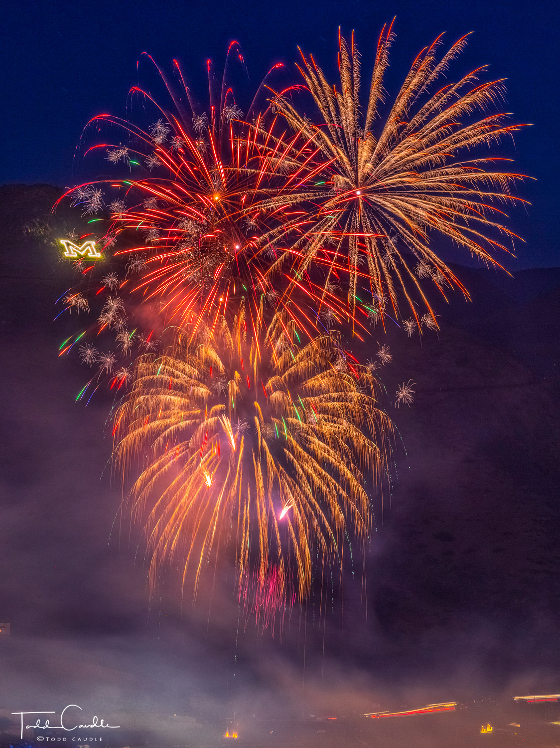 Fireworks burst in the air in front of Mount Zion and the Colorado School of Mines "M" logo.