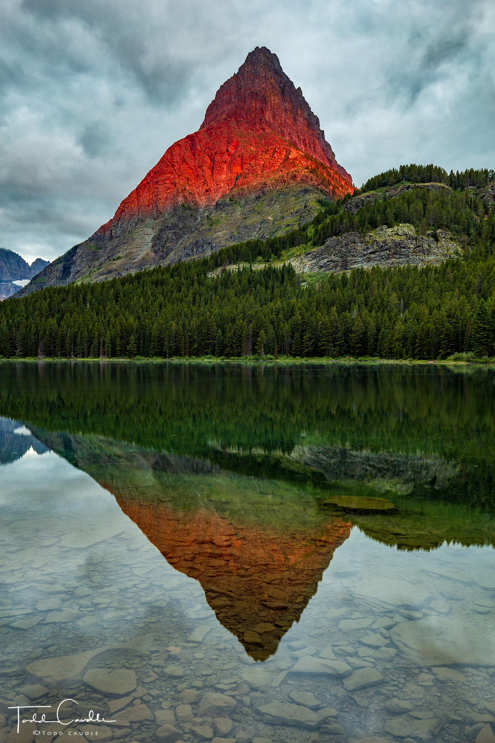 A fleeting moment of alpenglow light at sunrise illuminates a dramatic peak bordering Swiftcurrent Lake.