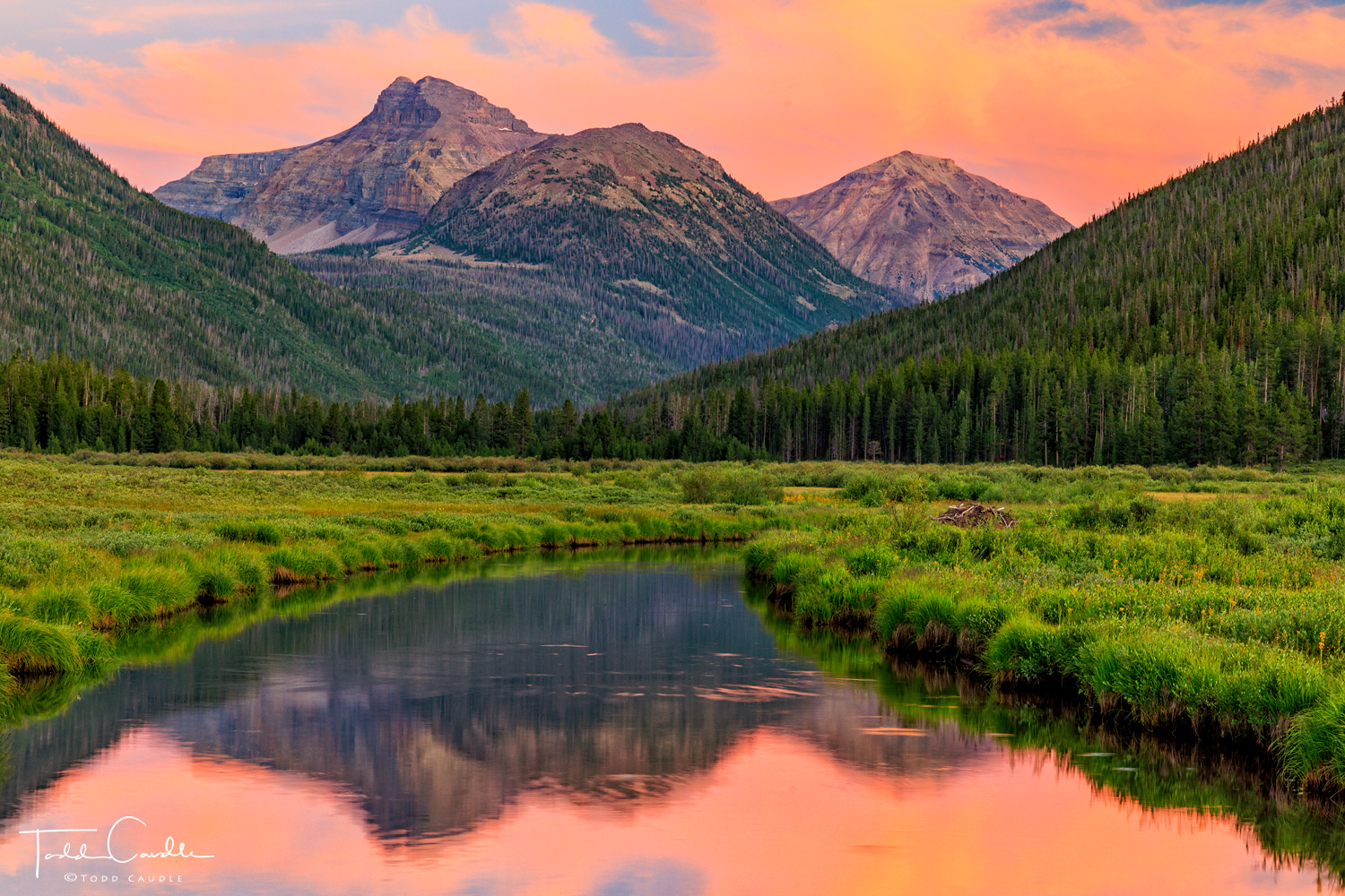 Dramatic sunset colors alight over Ostler Peak and Spread Eagle Peak in the Uinta Mountains, all reflected in a calm meander...