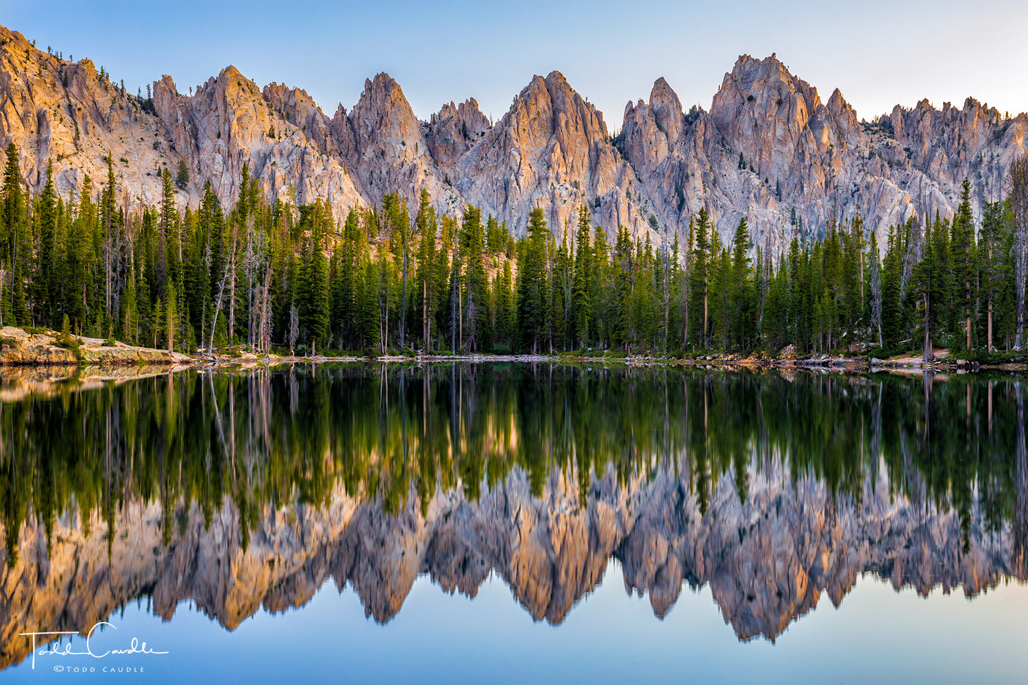 A serrated ridge in the Sawtooths Wilderness reflects in a lake at sunrise.