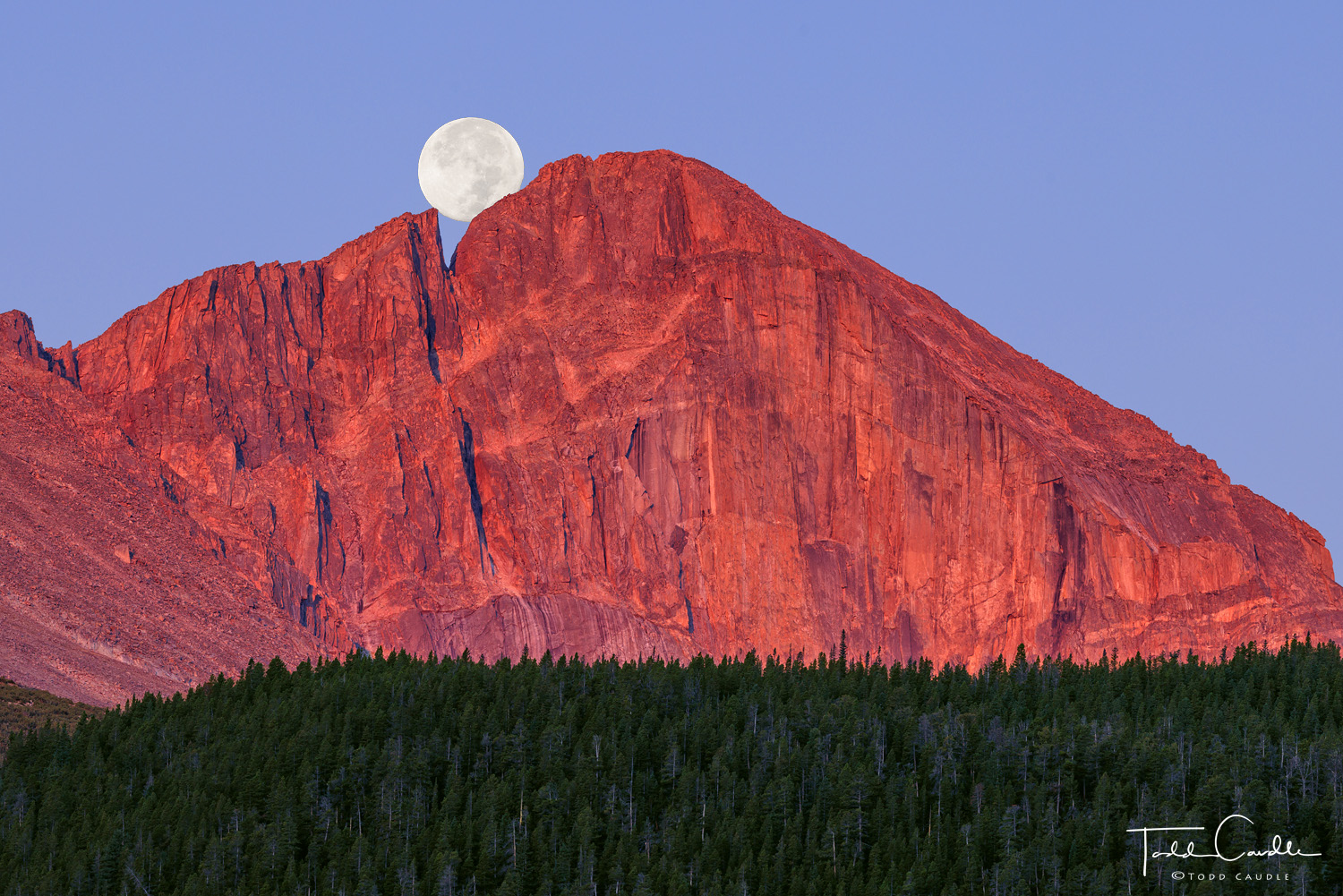 Alpenglow sunrise light paints The Diamond on Longs Peak in red hues as the moon sets behind The Notch.